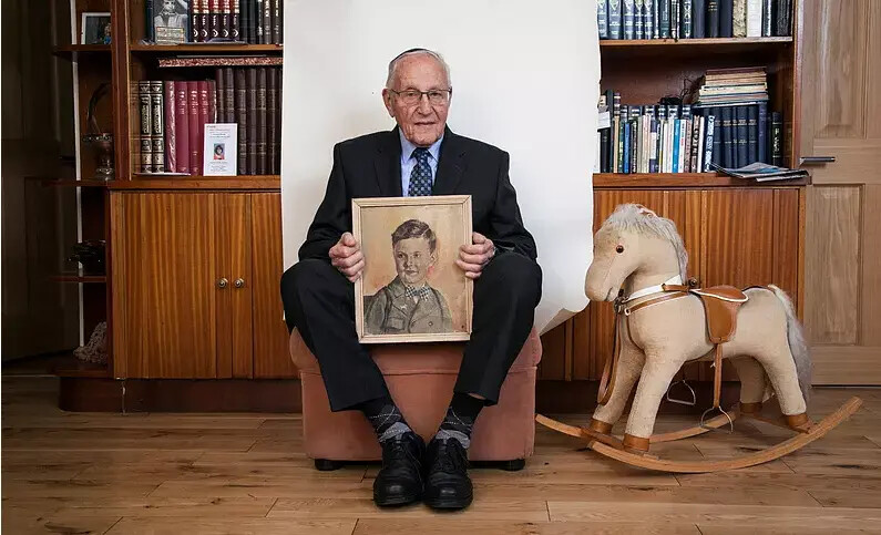 older man seated next to rocking horse and holiding photo