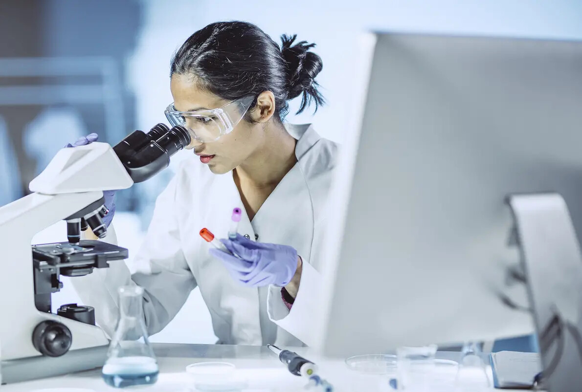 female scientist wearing goggles and looking intro microscope