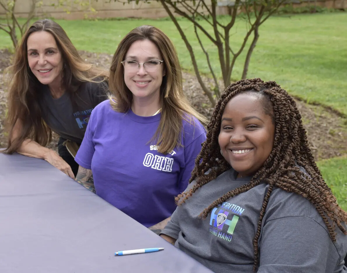 3 girls seated at table outside with middle girl in purple