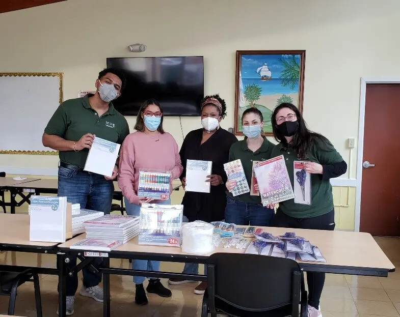 five people displaying art supplies in back of table