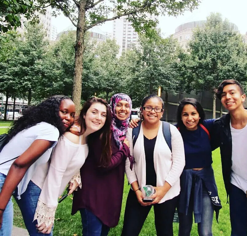 6 students outside with trees and building in background