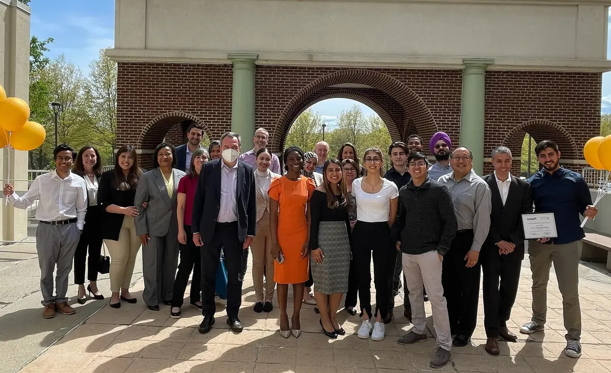 group of adults and students outside with arches behind them