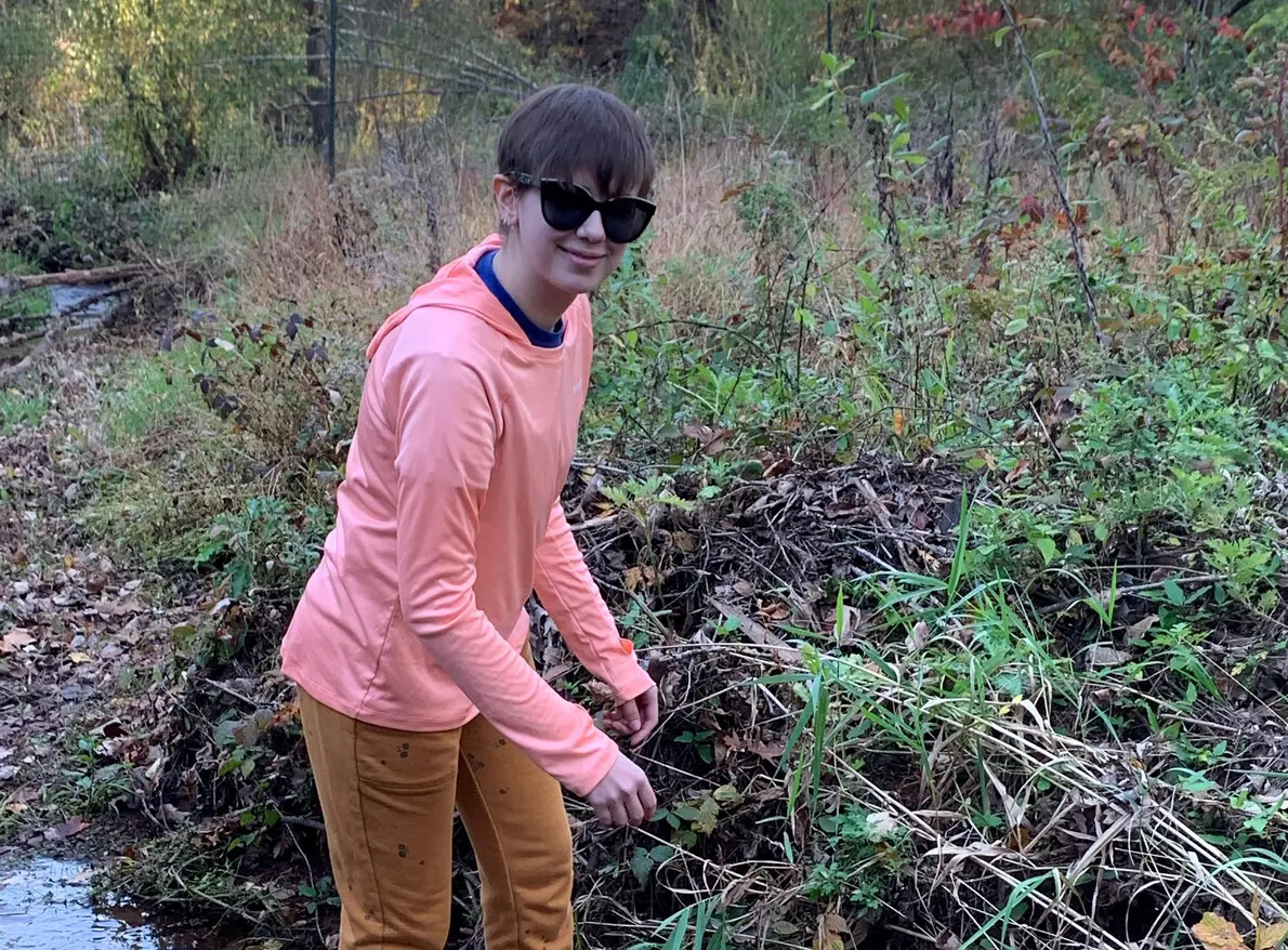 student in sunglasses in stream with brush