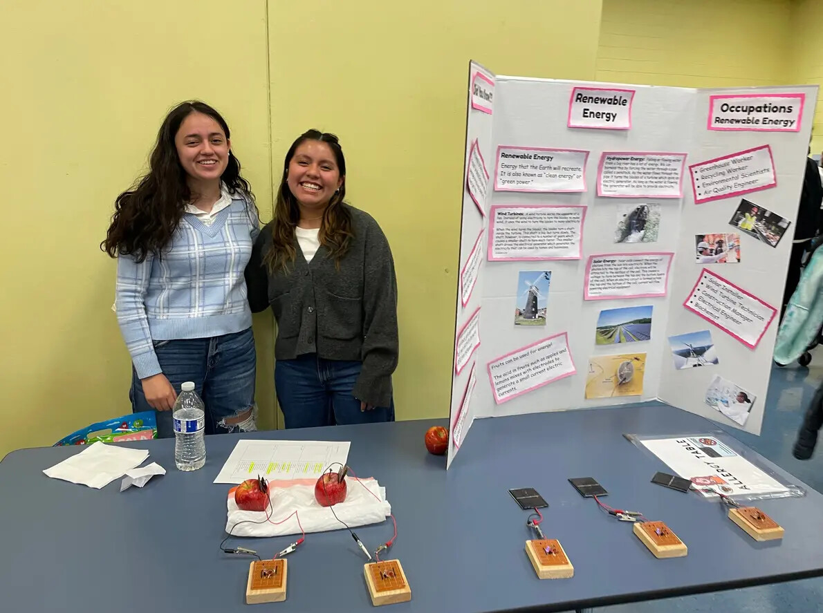 2 female students standing next to poster board on table