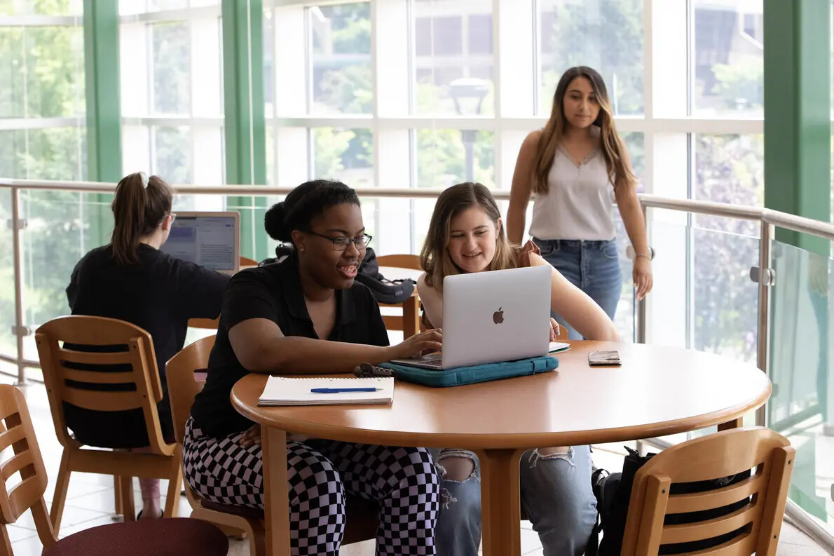 female students at laptop, one walking, and one from back