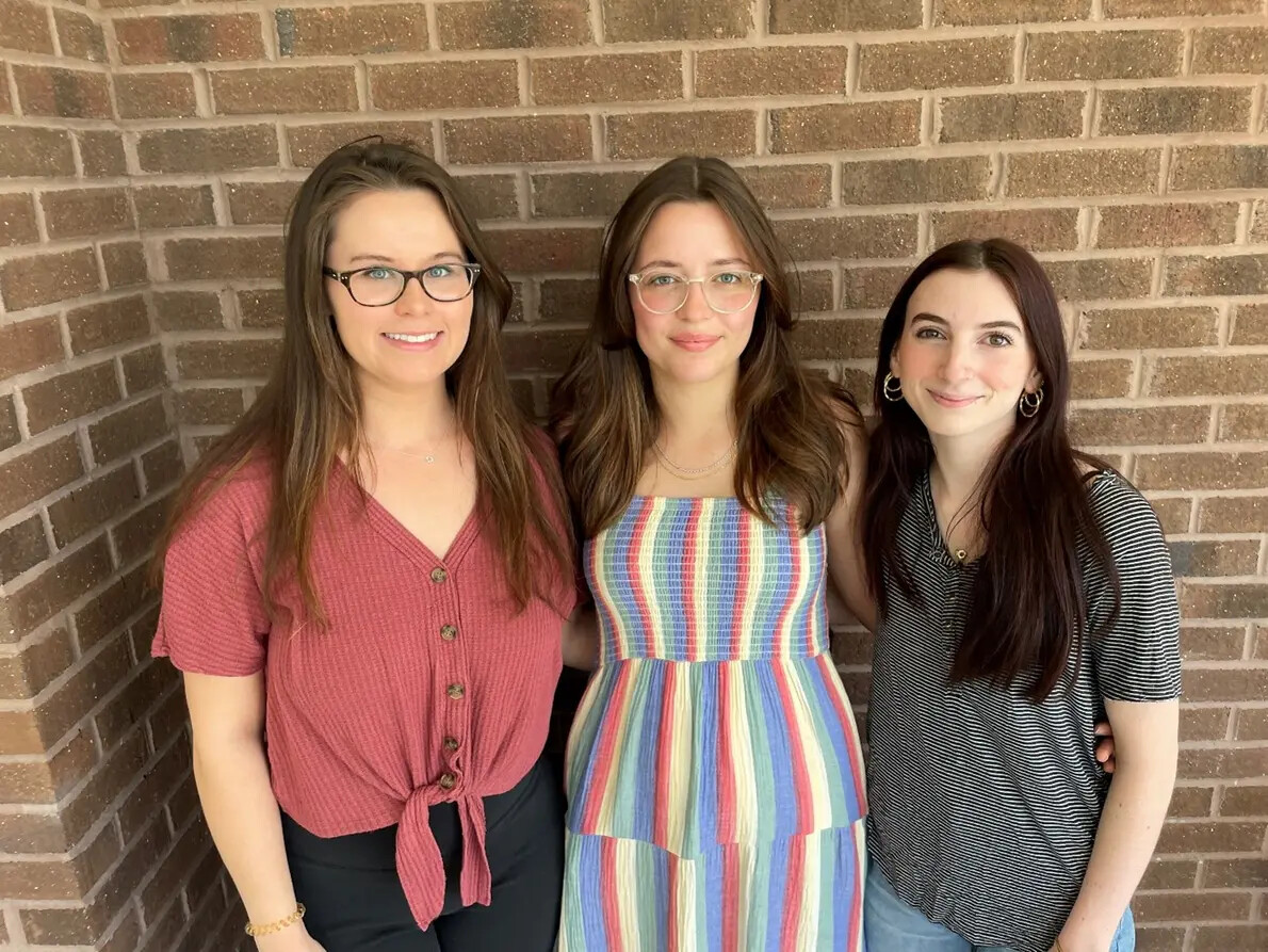 3 female students and 2 with glasses against brick wall