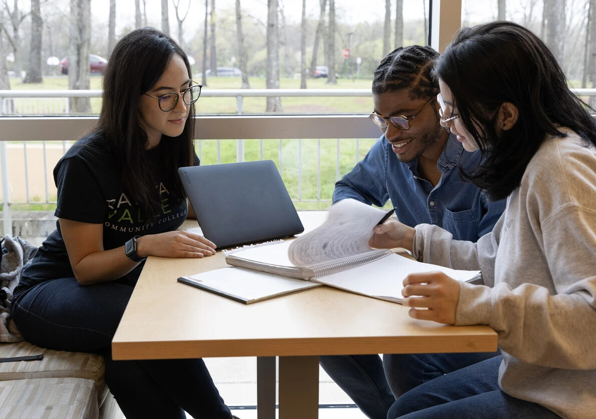 3 students sitting at table with window behind them