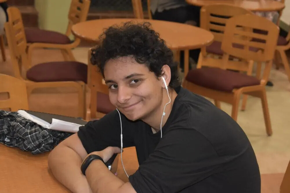 curly haired male student with headphones in ears