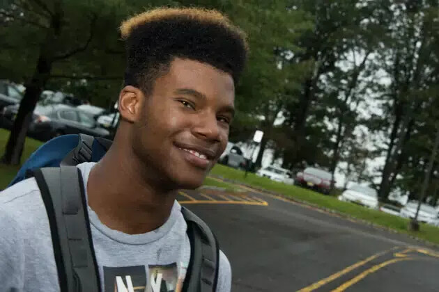 young man outside wearing grey tshirt and carrying backpack