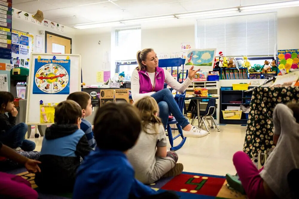 teacher on chair in classroom and backs of students