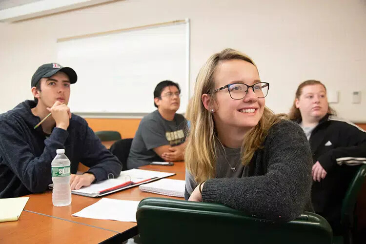 4 students in classroom with one smiling in front