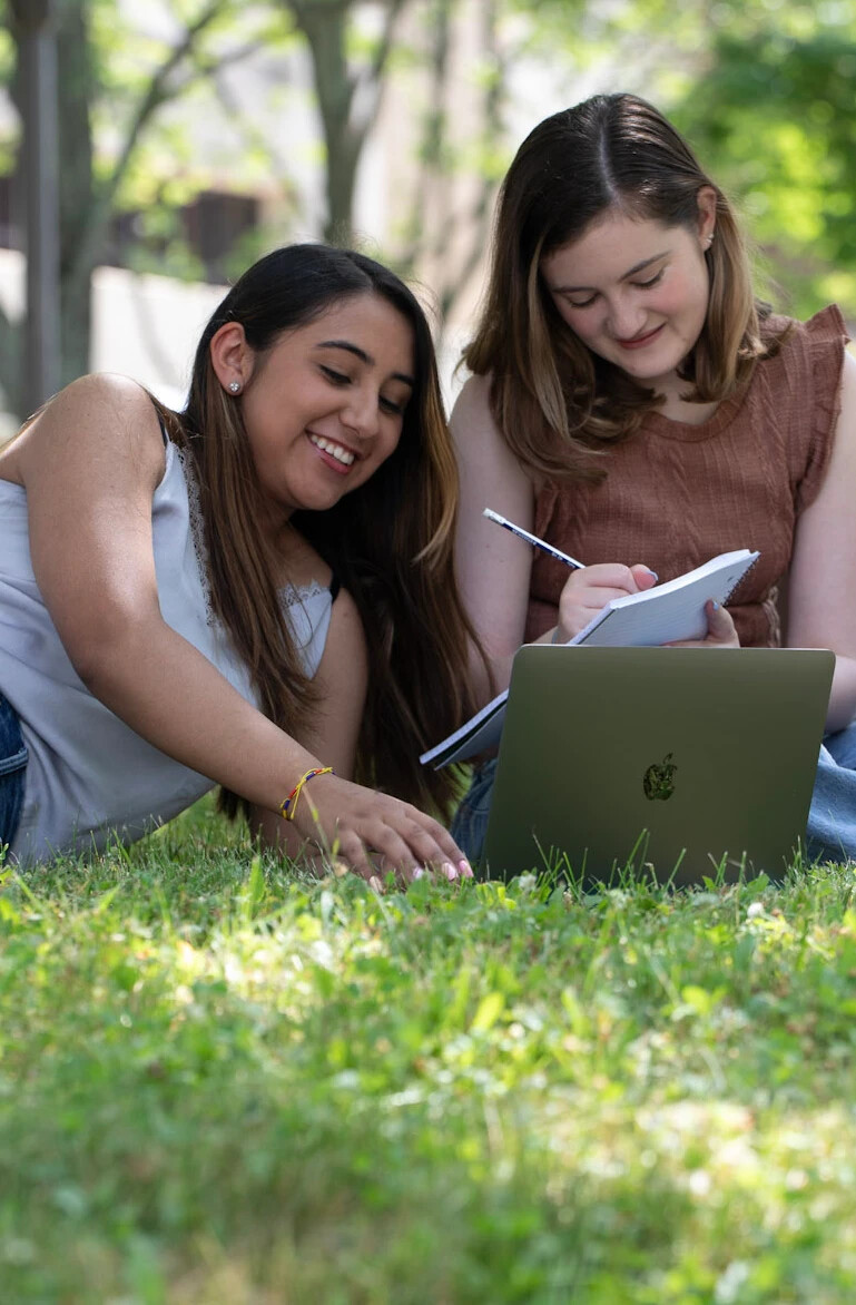 2 students working on laptops in courtyard