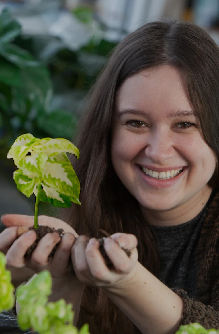 female student in greenhouse with a plant and dirt in her hands