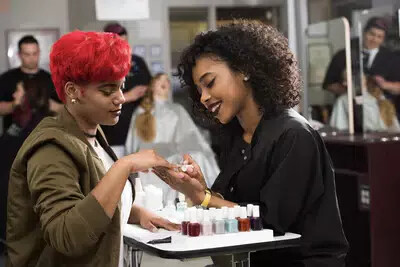 student with bright red hair getting manicure by another student
